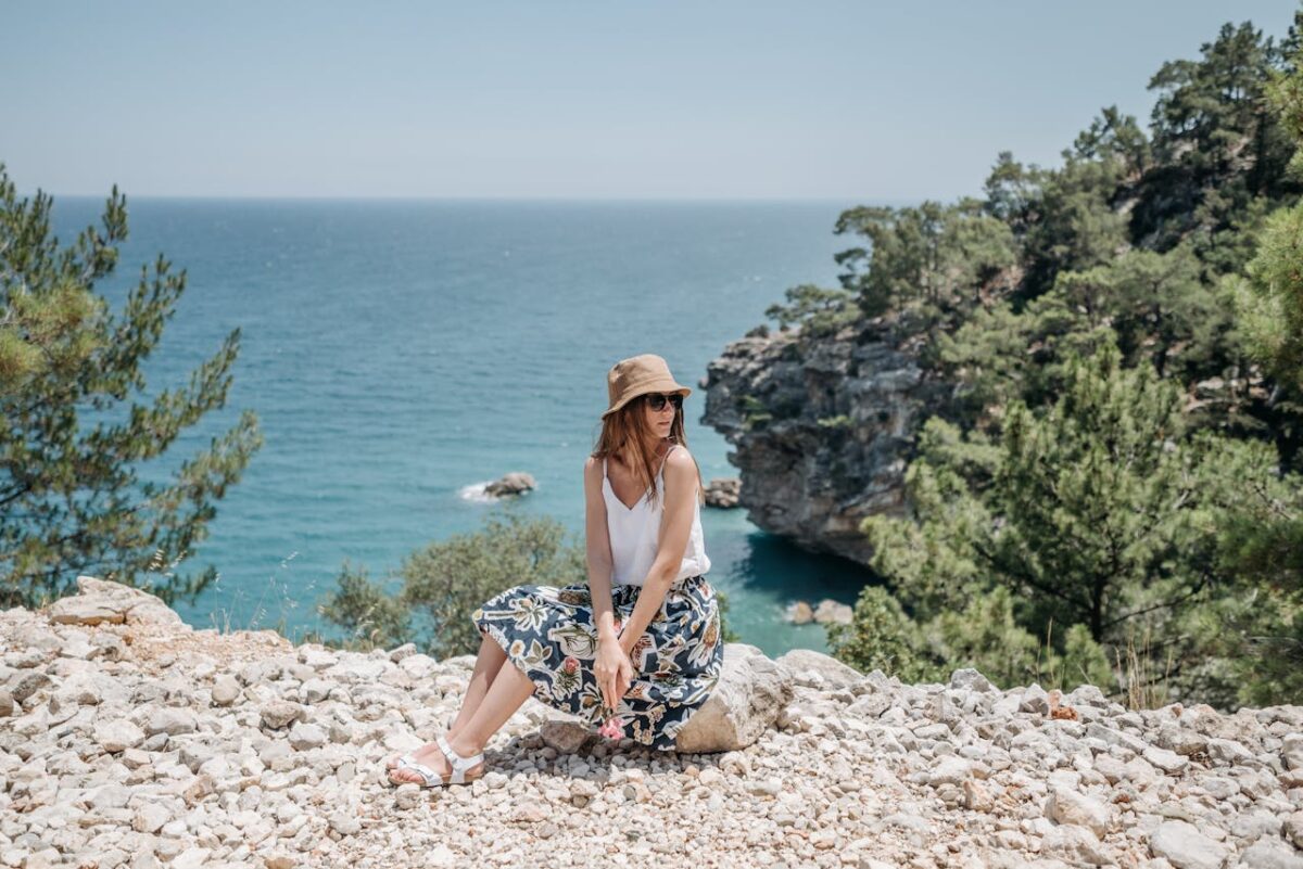 Woman in summer attire sitting by a scenic coastal view.